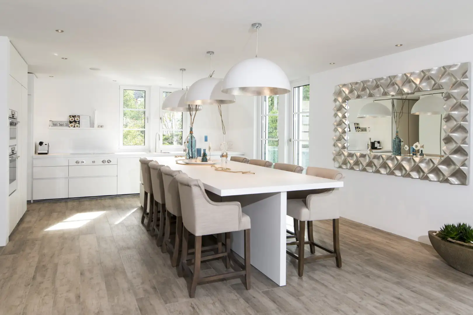 Moderne, weisse Küche mit grossem Inselbereich und einem großen Spiegel an der Wand.